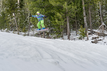 Snowboarder freerider jumping from a snow ramp on a background of forest and mountains.の写真素材