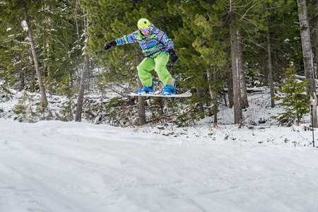 Snowboarder freerider jumping from a snow ramp on a background of forest and mountains.の写真素材