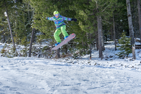 Snowboarder freerider jumping from a snow ramp on a background of forest and mountains.の写真素材