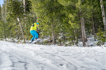 Snowboarder freerider jumping from a snow ramp on a background of forest and mountains.の写真素材
