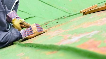 Worker sitting on the roof and scraping of fading paintの写真素材