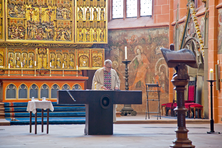 GERMANY, FRANKFURT AM MAIN - May 07.2014: Imperial cathedral of saint Bartholomew. A pastor reads prayer on a background an ancient iconostasisのeditorial素材