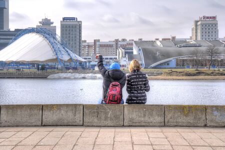 BELORUSSIA, MINSK - March 11.2017: Fellow and girl sit on the parapet of the river Svislachのeditorial素材