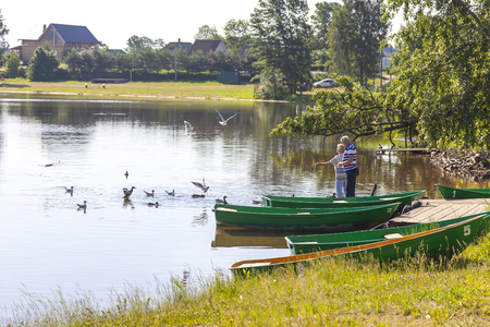 VALDAY, RUSSIA - June 08.2019: An elderly couple feeding birds on the shores of Valdayskoye Lakeのeditorial素材