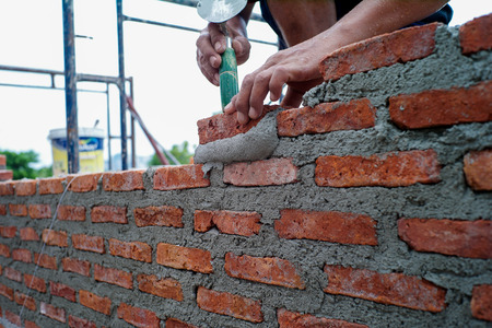 Worker uses the trowel for installing the red bricks on the wall at the house under construction.の写真素材