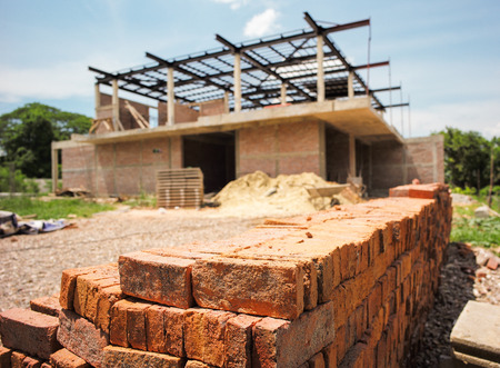 Pile of red bricks with blurred house under construction.の写真素材