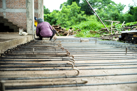 Worker doing the steelwork for reinforcement of the concrete structure with blurred worker in background at the construction siteの写真素材
