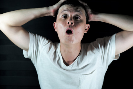 Portrait Asian man act surprised by putting his hands on his head with isolated black backgroundの写真素材