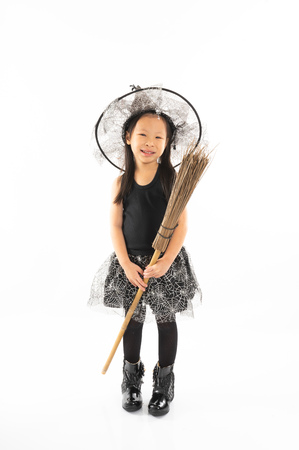 Portrait Asian little girl dressing in cute witch riding the broom for Halloween costume with funny face and isolated backgroundの写真素材