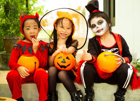 Portrait of happy sisters in Halloween costume sitting in front of the door and waiting for playing Trick or treat. Happy Halloween daysの写真素材