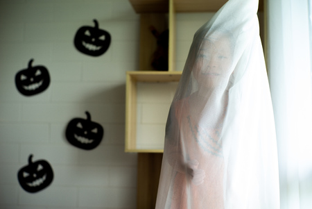 Portrait Asian little girl playing and hiding in the white clean curtain with Halloween decoration in background.の写真素材