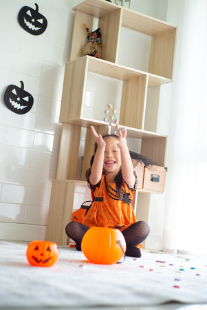 Portrait Asian little girl throwing and eating candy and chocolate from trick or treat with Halloween theme in backgroundの写真素材