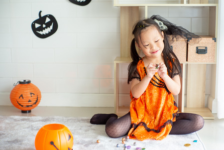 Portrait Asian little girl throwing and eating candy and chocolate from trick or treat with Halloween theme in backgroundの写真素材