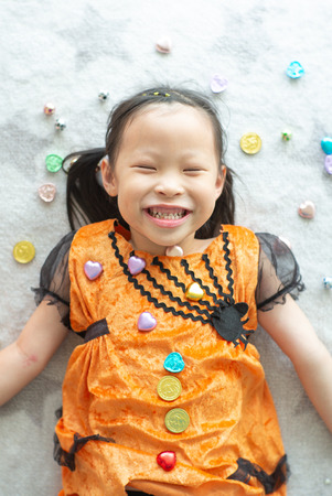 Portrait Asian little girl throwing and eating candy and chocolate from trick or treat with Halloween theme in backgroundの写真素材