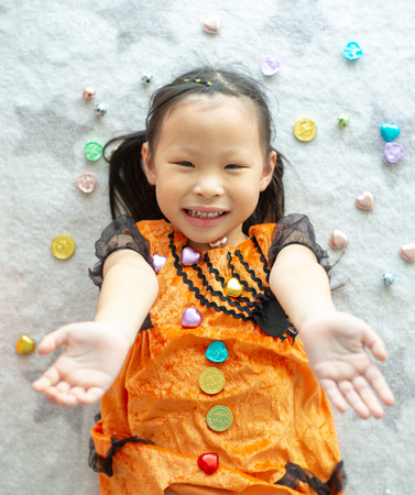 Portrait Asian little girl throwing and eating candy and chocolate from trick or treat with Halloween theme in backgroundの写真素材