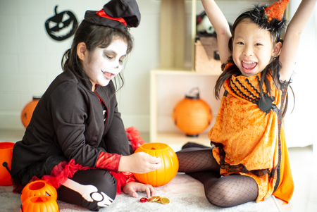 Portrait of two happy sisters in the Halloween costume sharing the candy and chocolate from trick or treatの写真素材