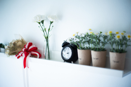 Vintage alarm clock puts on the white wooden shelf decorated by the blossom flowers in the pottery...
