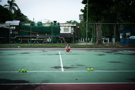 Portrait Asian girl sits on the tennis court after playing hard with ancient train in backgroundの写真素材