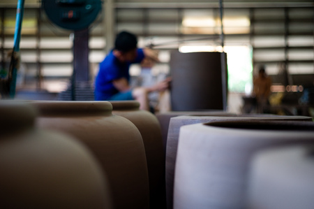 Closeup picture of traditional clay pottery in the factory with blurred worker working in backgroundの写真素材