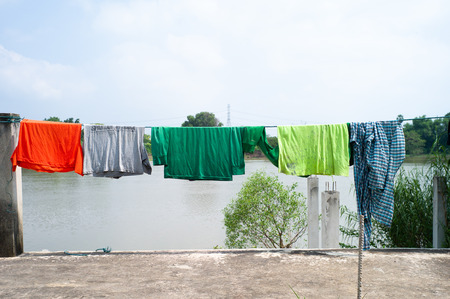 Old wet clothes hanging on the clothsline with blue sky and river in backgroundの写真素材