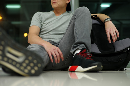 Portrait of unidentified man sitting on the floor of airport terminal with his backpackの写真素材