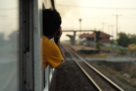 Blurred back portrait of  man taking the picture at camera from the outside of train window with blurred track and landscape of natural backgroundの写真素材