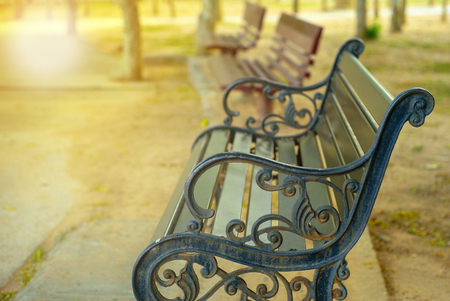 Closeup rusted steel vintage bench with blurred wooden benches in background at outdoor public parkの写真素材