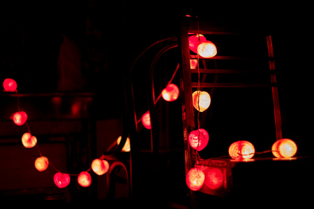 Closeup heart shape of led lights line hanging on the wooden chairs decorated in the darkroomの写真素材