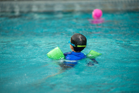 Back portrait little boy in swimsuit with life ring in his arms floating in the swimming pool