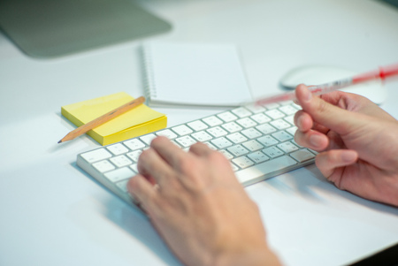 Selective focus on white keyboard of desk top with blurred motion of hands spinning the pencil in foreground with notepad and pencil in backgroundの写真素材
