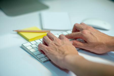 Closeup selective focus on hands of businessman typing on the keyboard with defocused stationaries in backgroundの写真素材