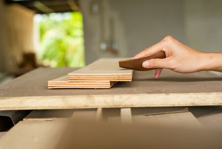 Selective focus on a hand of carpenter holds the sand paper and scrubs on the wood surface at the...