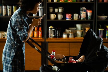 Bangkok, Thailand : June 26, 2019 - Selective focus on cute baby in cart looks at parent and takes a picture by mobile phone in the coffee shopのeditorial素材