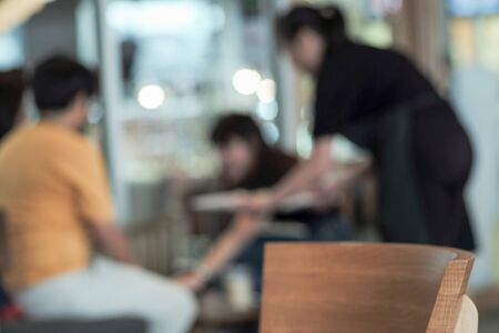 Defocused waitress serves the food to customers in restaurant with bokeh lights in backgroundの写真素材