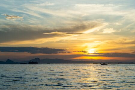 Silhouette of moving long tail boat with shadow of island  and orange light of sunrise in background. Landscape of calm sea in early morningの写真素材