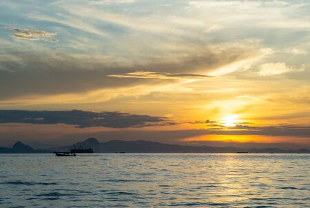 Silhouette of moving long tail boat with shadow of island  and orange light of sunrise in background. Landscape of calm sea in early morningの写真素材