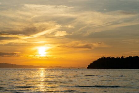 Landscape of calm sea with silhouette of island and orange light of sunriseの写真素材