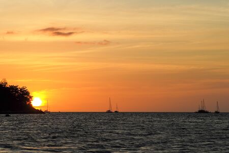 Silhouette of island and yacht boats on the horizontal line with light of sunset and twilight sky in backgroundの写真素材