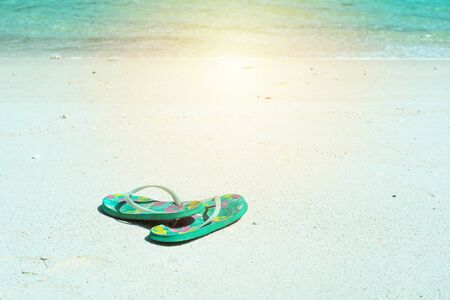 Closeup pair of old sandals put on the white sand beach with blurred sea surfing into the coast backgroundの写真素材