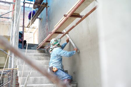 Group of workers stand on the steel scaffolding and builds plastered cement wall in the house under constructionの写真素材