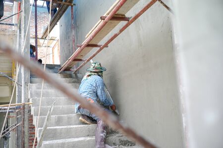 Group of workers stand on the steel scaffolding and builds plastered cement wall in the house under constructionの写真素材