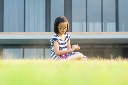 Closeup portrait of Asian girl with eyeglasses sits on the grass field in the backyard with blurred modern house in backgroundの写真素材