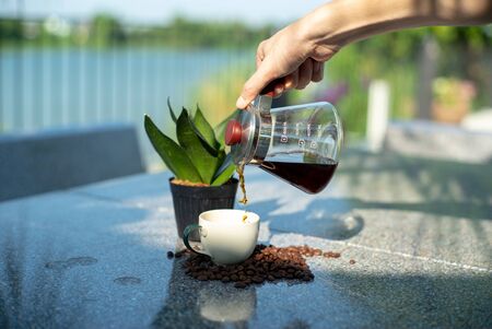 Hand of barista pouring the coffee from the glass jar into the cup at the outdoor gardenの写真素材