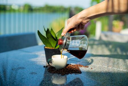 Hand of barista pouring the coffee from the glass jar into the cup at the outdoor gardenの写真素材