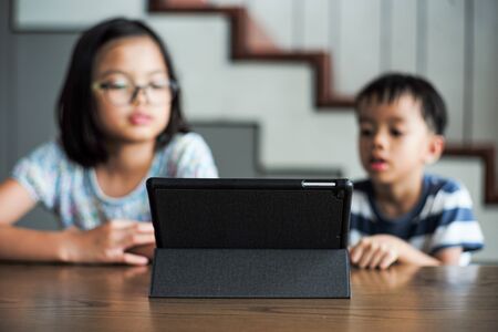 Selective focus on the tablet on the wooden table with blurred students learning at homeの写真素材