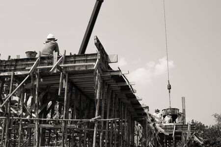 Monochrome picture of workers pouring the mixed cement from the steel bucket hanging from the craneの写真素材