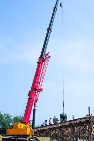 High angel view group of workers pouring the mixed cement from big steel bucket hanging from the crane.の写真素材