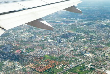 Closeup wing of airplane while flying in the air with cityscape belowの写真素材