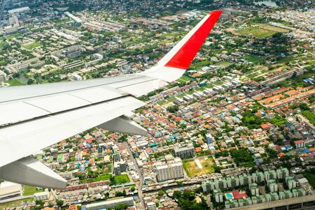 Closeup wing of airplane while flying in the air with cityscape belowの写真素材