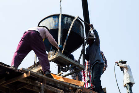 High angel view group of workers pouring the mixed cement from big steel bucket hanging from the crane.のeditorial素材